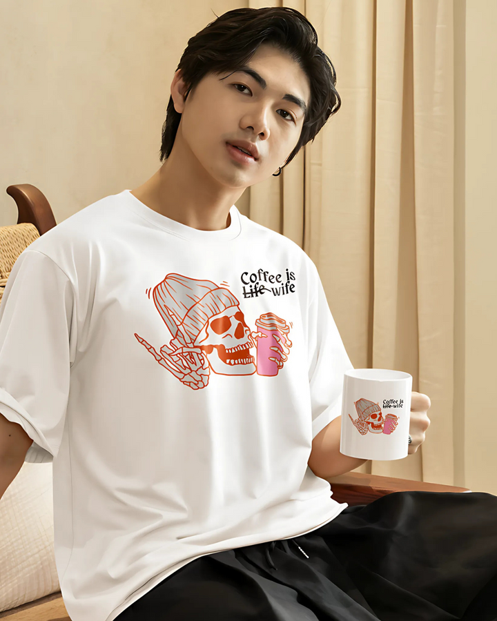 Person wearing a white t-shirt with a graphic design and holding a mug.